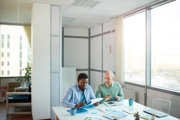 Foto brede hoekmening van afro-amerikaanse jonge man overleg met volwassen manager zittend aan tafel in kantoor, kopieer ruimte