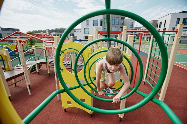 Foto brede hoekmening van jonge jongen spelen in jungle gym op kleurrijke speelplaats kopieerruimte