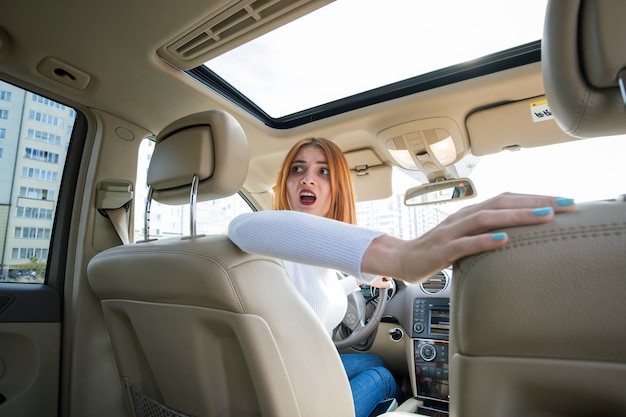 Brede hoekmening van jonge roodharige vrouwenbestuurder die een auto drijft die erachter eruit ziet.