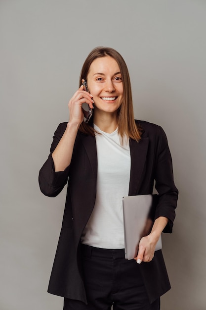 Breed glimlachende vrouw praat over de telefoon terwijl ze haar laptop vasthoudt