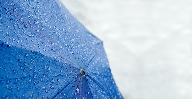 Breed scherm van regendruppels op blauwe paraplu met wazige weg op regenachtige dag