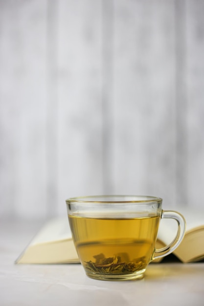 Brewed herbal green tea in a transparent cup in front of an open book on a light background