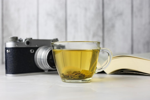 Brewed herbal green tea in a transparent cup next to an open book and a vintage camera