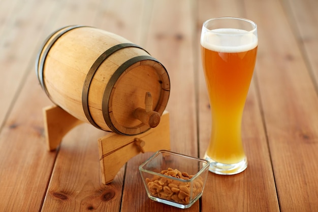 brewery, drinks and alcohol concept - close up of draft lager beer in glass, peanuts and wooden barrel on table