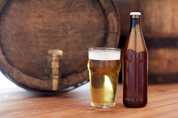 brewery, drinks and alcohol concept - close up of old beer barrel, glass and bottle on wooden table