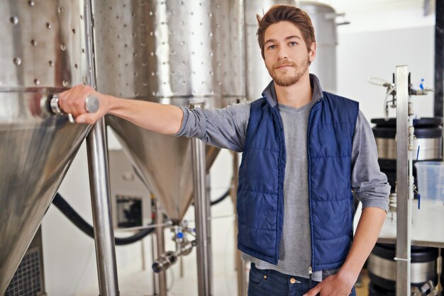 brewery man and manufacturing machine with portrait for craft beer container or production process in factory industrial industry worker and smile in distillery with tank for brewing in warehouse