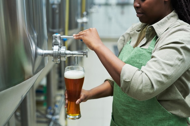Работник пивоварни наполняет стакан пивом