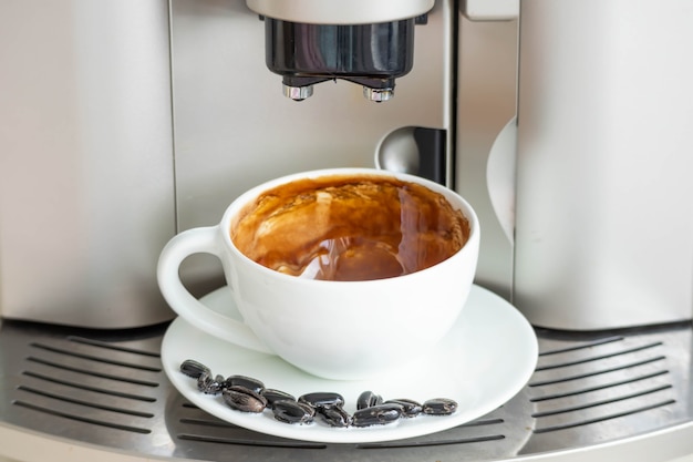 Brewing fresh coffee from your espresso machine. Budget coffee maker. White cup decorated with coffee beans.