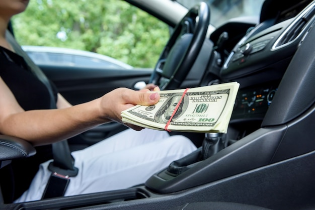 Bribe concept. Female hands giving dollar bundle inside car close up