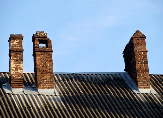 Brick chimneys on the slate roof of an old house Red with smoke stack with damage and blue sky