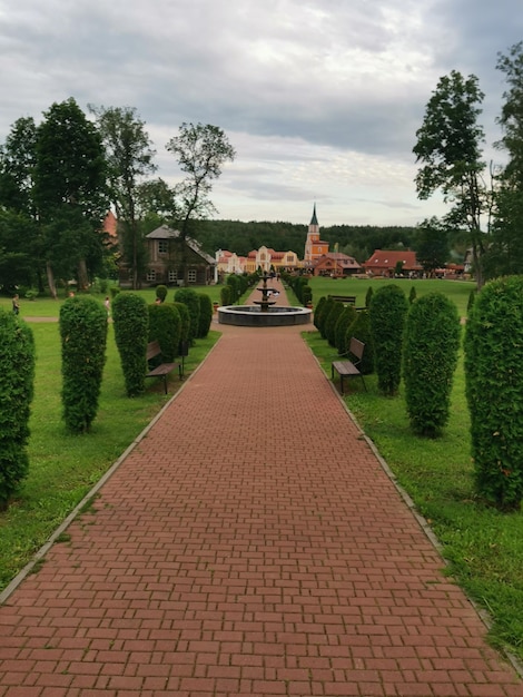 a brick walkway leads to a park with a fountain in the middle.