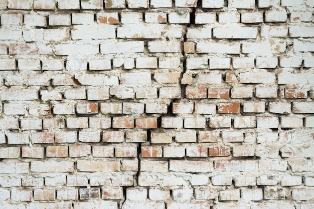 Brick wall with a big crack in the middle. Wall made of red brick and painted with white ink cracked vertically background