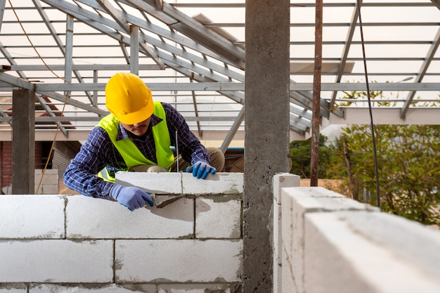 Bricklayer builder working with autoclaved aerated concrete blocks. Walling, installing bricks on construction site, Engineering and constructions concepts.