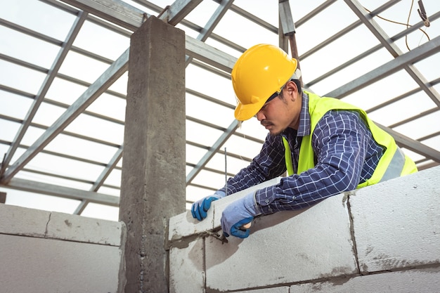 Bricklayer builder working with autoclaved aerated concrete blocks. Walling, installing bricks in construction site