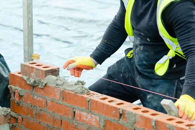 Bricklayer laying bricks on mortar on new residential house construction