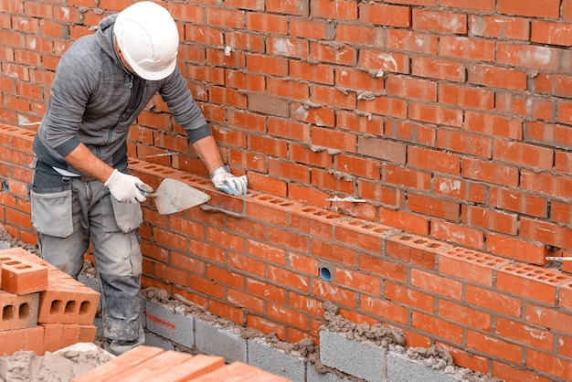 Photo bricklayer laying bricks on mortar on new residential house construction