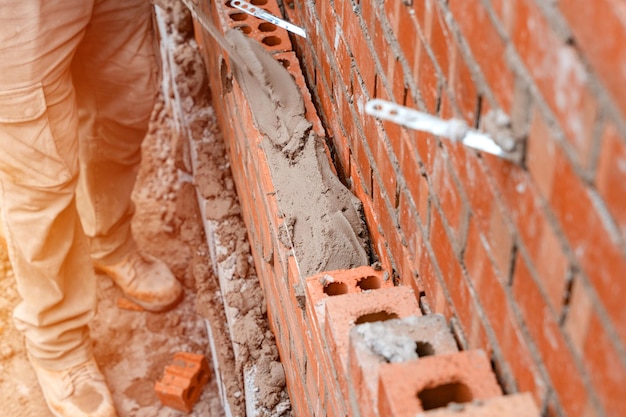 Bricklayer laying bricks on mortar on new residential house construction