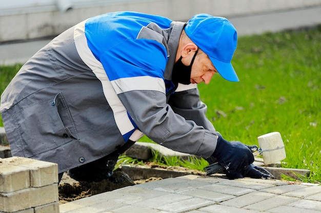 Bricklayer lays paving slabs outside working man performs\
landscaping builder lays out sidewalk with stone blocks