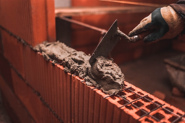 Bricklayer puts bricks to make a wall