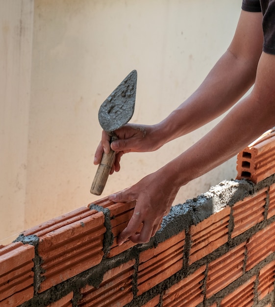 Bricklayer worker installing brick masonry on exterior wall.