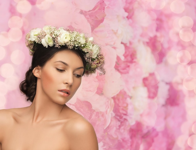 Bridal, spring and beauty concept - young woman wearing wreath of flowers on floral background