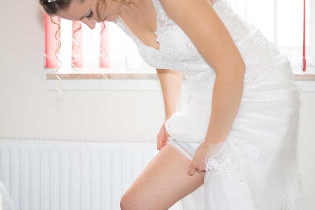 Bride adjusting wedding dress in room