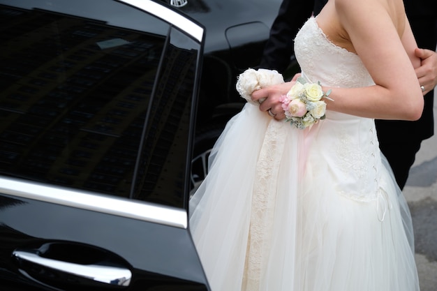 写真 黒い車に乗り込む美しい白いドレスを着た新郎新婦。車の隣の新婚夫婦。