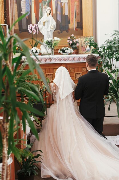 写真 結婚式中に聖母マリア像にひざまずいて祈る新郎新婦 スピリチュアルなカップル 教会での結婚 感情的なロマンチックな瞬間