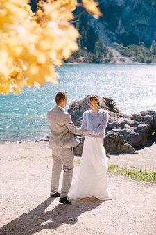 イタリア​の​ブラーイエス湖​で​燃える​ような​黄色​の​葉​を​持つ​秋​の​木の下​で​新郎​新婦