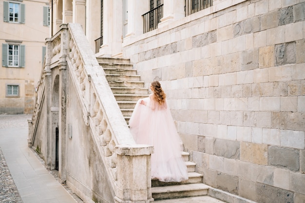 美しいドレスを着た花嫁がイタリアのベルガモにある古代の建物の階段を登る