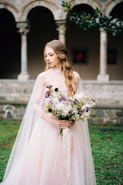 Bride in a beautiful dress with a bouquet of flowers in a green garden against the scene of an