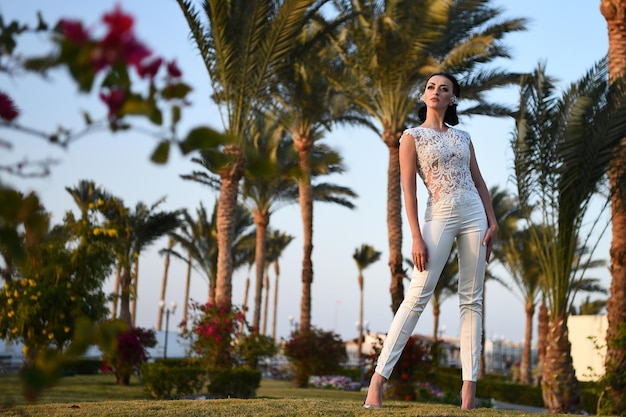 Sposa in abito ricamato bel matrimonio o panno giovane donna all'aperto con palme e cielo blu soleggiato