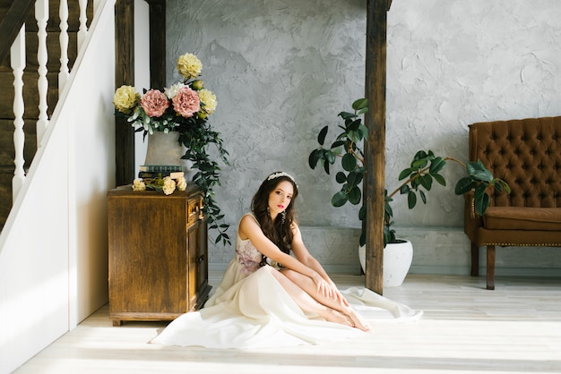 The bride in a beautiful white wedding dress sits on the floor barefoot
