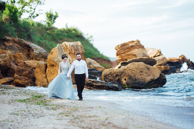 bride in a blue dress walk along the ocean shore