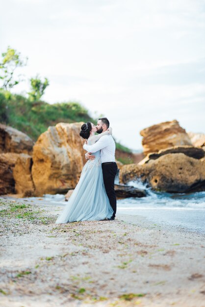 bride in a blue dress walk along the ocean shore