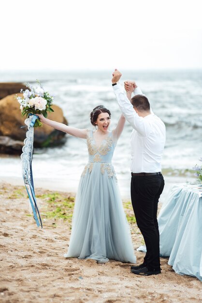 bride in a blue dress walk along the ocean shore