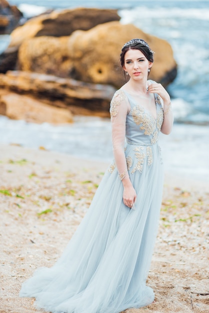 Bride in a blue light dress walking along the ocean