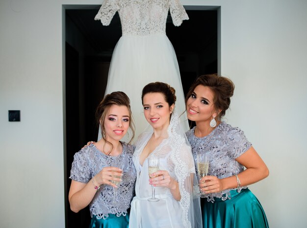 Bride and bridesmaids in blue dresses drink champagne before a wedding dress