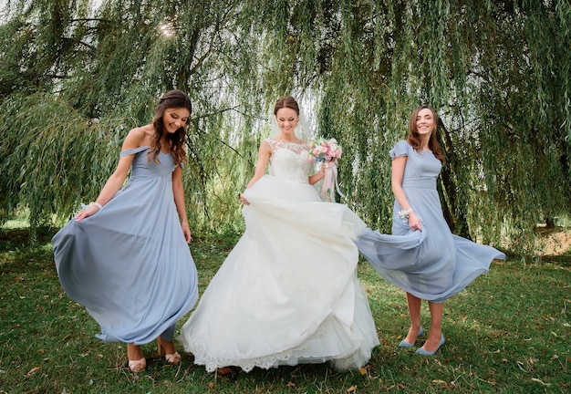 bride and bridesmaids in blue dresses whirl on geen lawn