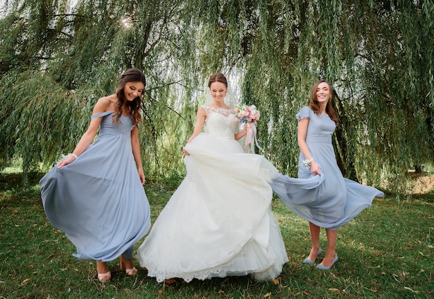 Bride and bridesmaids in blue dresses whirl on geen lawn