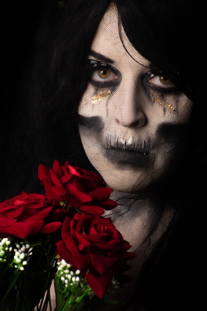 Photo bride cadaver with black veil holding a bouquet of red roses, black background, low key portrait, selective focus.