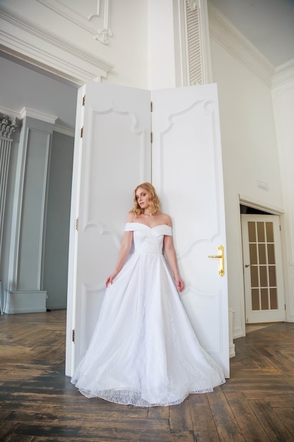 A bride in a chic wedding dress stands near the door and looks to the side thoughtfully