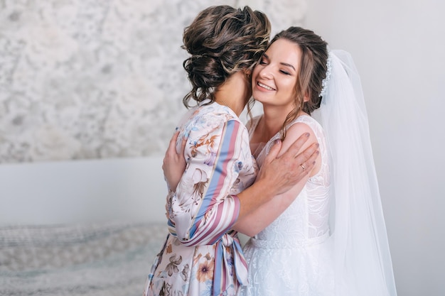 Bride closes her eyes hugging mother tender mom congratulates\
the bride with a marriage and hugs happy bride with mother on\
background wall in home bride morning preparation