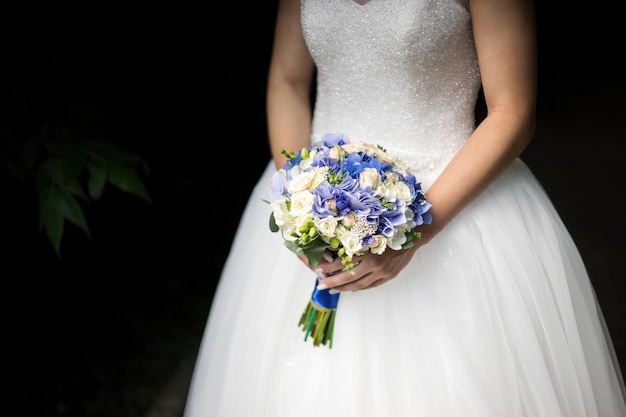 Невеста в платье стоит в зеленом саду и держит свадебный букет цветов и зелени