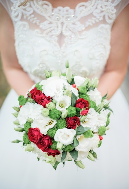 レースのコルセットとドレスの花嫁は、彼女の胸の前に白と赤の花束を保持