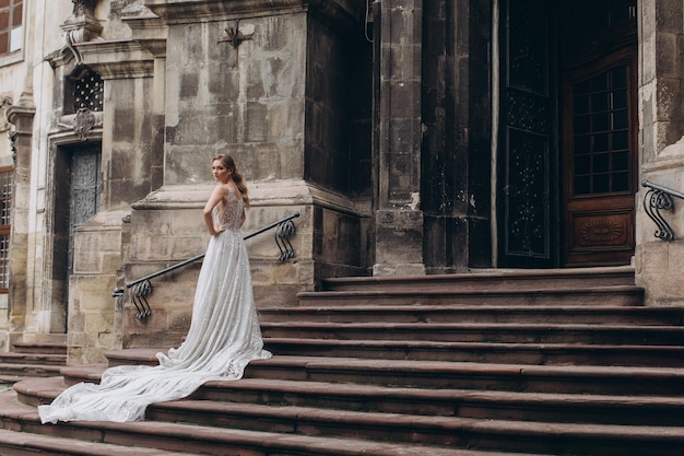 Bride in dress with long train stands before an old Gothic church