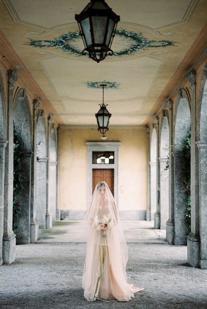 Sposa in abito con velo cammina con un bouquet lungo la terrazza di un'antica villa