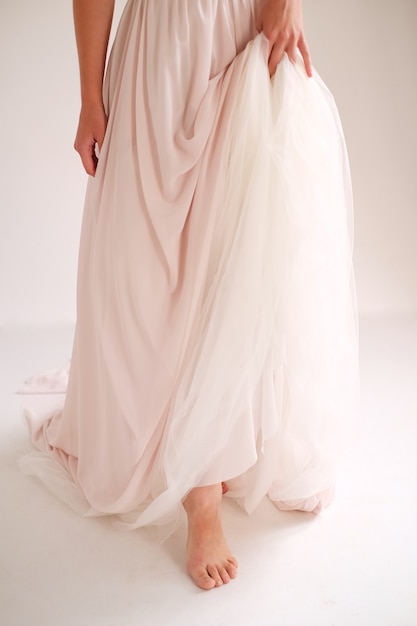 Bride in an elegant silk dress stands and holds the dress by the edge belt