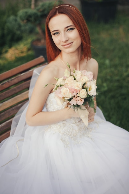 Bride in elegant wedding gown sits on stone bench