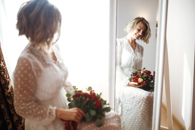 Невеста в элегантном белом платье смотрит в зеркало Невеста улыбается и позирует перед зеркалом